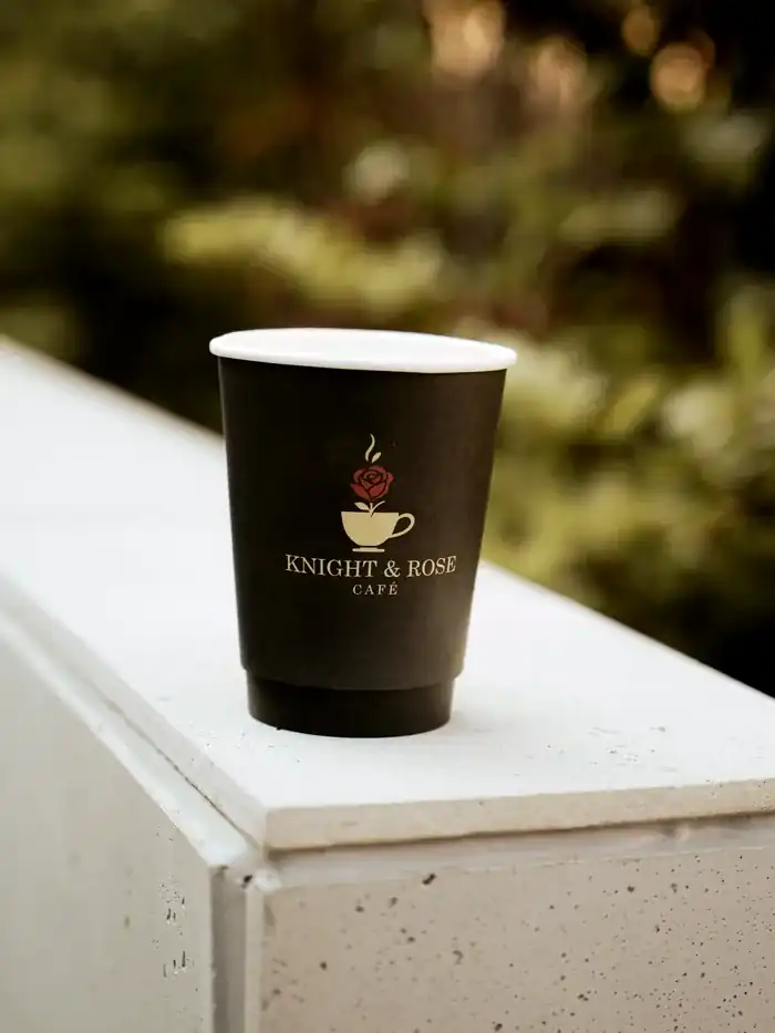 A Knight & Rose Café cup with its gold rose emblem, caught in warm afternoon light.
