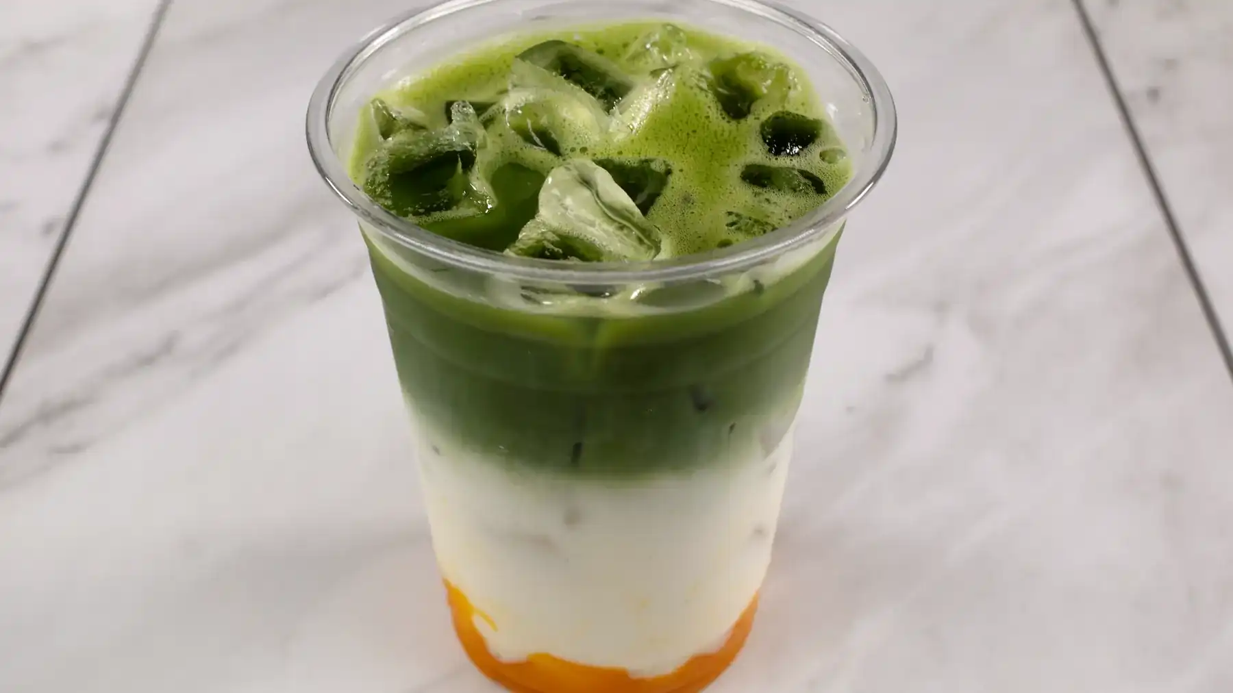 A bowl of ceremonial grade matcha being whisked with a bamboo chasen on a walnut table.