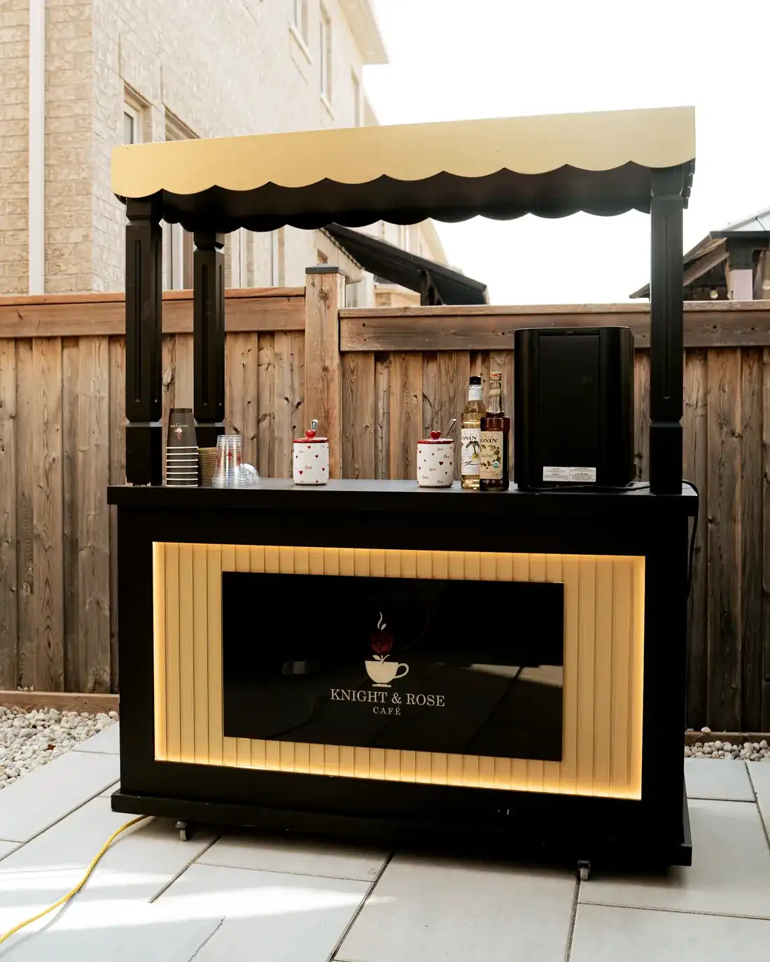 The Knight & Rose mobile café cart in black and gold, set up outdoors.